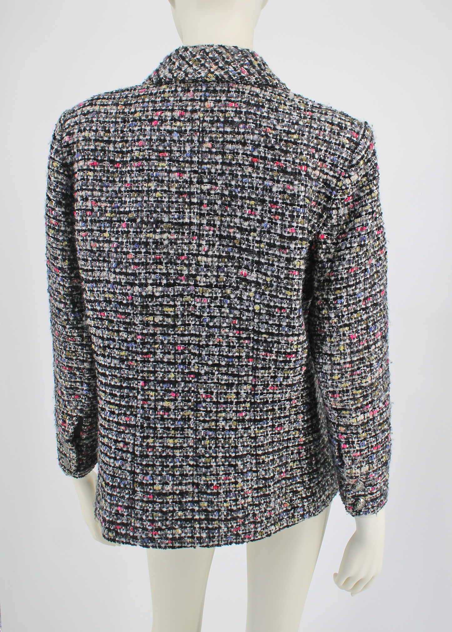Back view of the Black, white, and multicolor silk-blended tweed jacket with two slit pockets on the front, a notch collar and 'CC' buttoned cuffs. CC button closure at front. Lined in black Camellia printed silk and has a silver signature chain around the inside of the hemline.