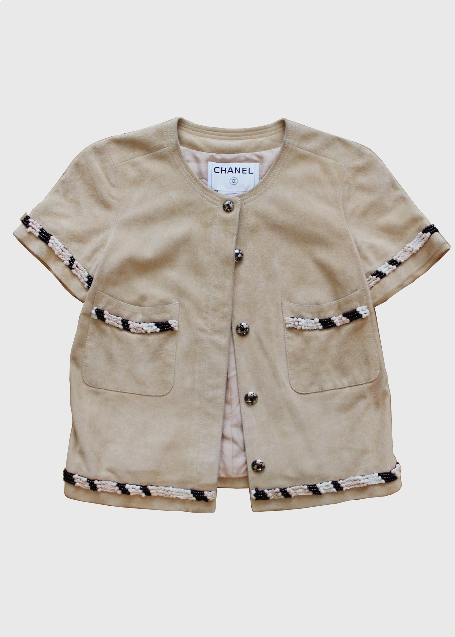 Cropped, short-sleeved suede jacket by Chanel, featuring globe-printed CC enameled buttons and beaded, threaded, and knotted trims throughout. Two front patch pockets