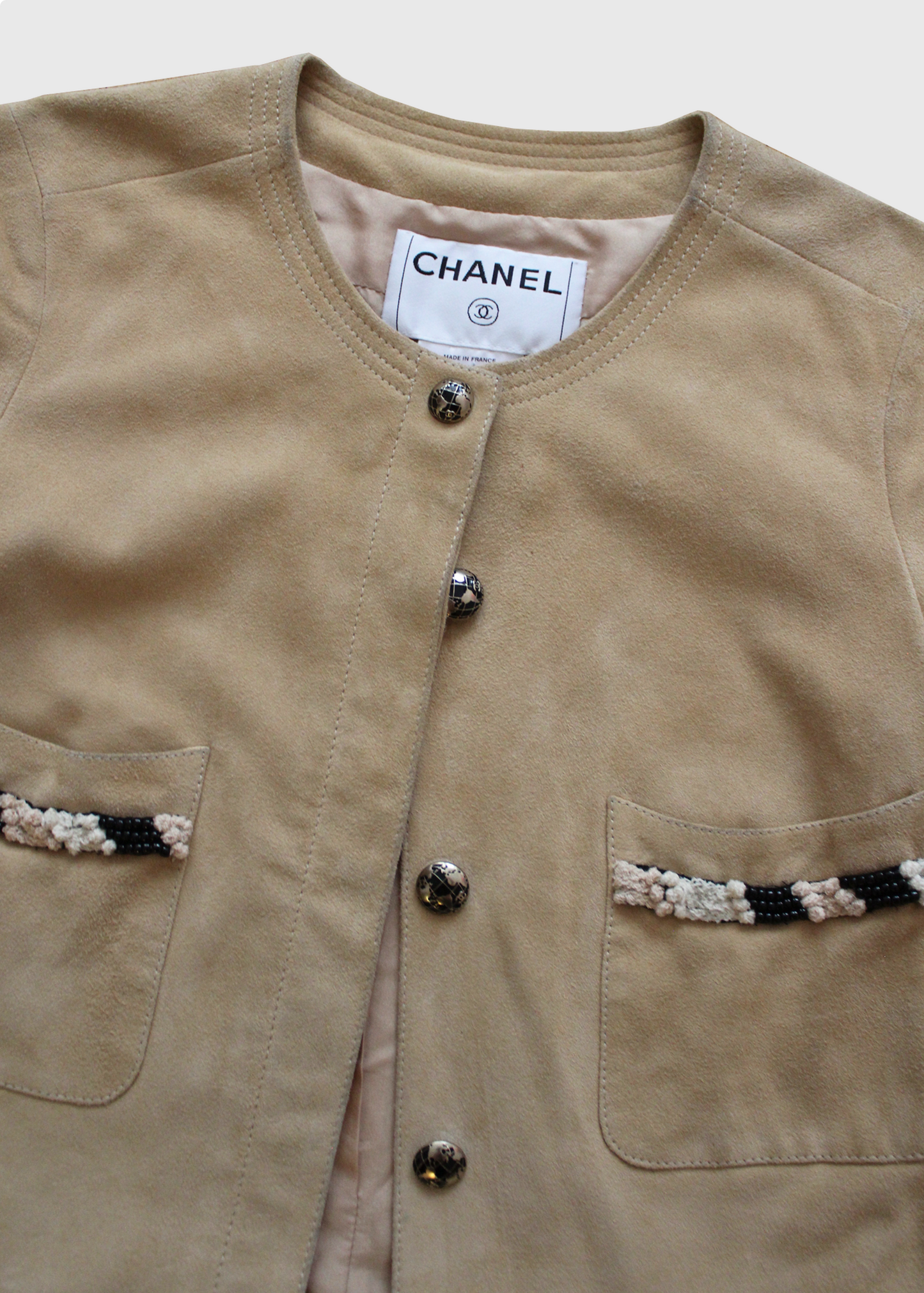 Cropped, short-sleeved suede jacket by Chanel, featuring globe-printed CC enameled buttons and beaded, threaded, and knotted trims throughout. Two front patch pockets
