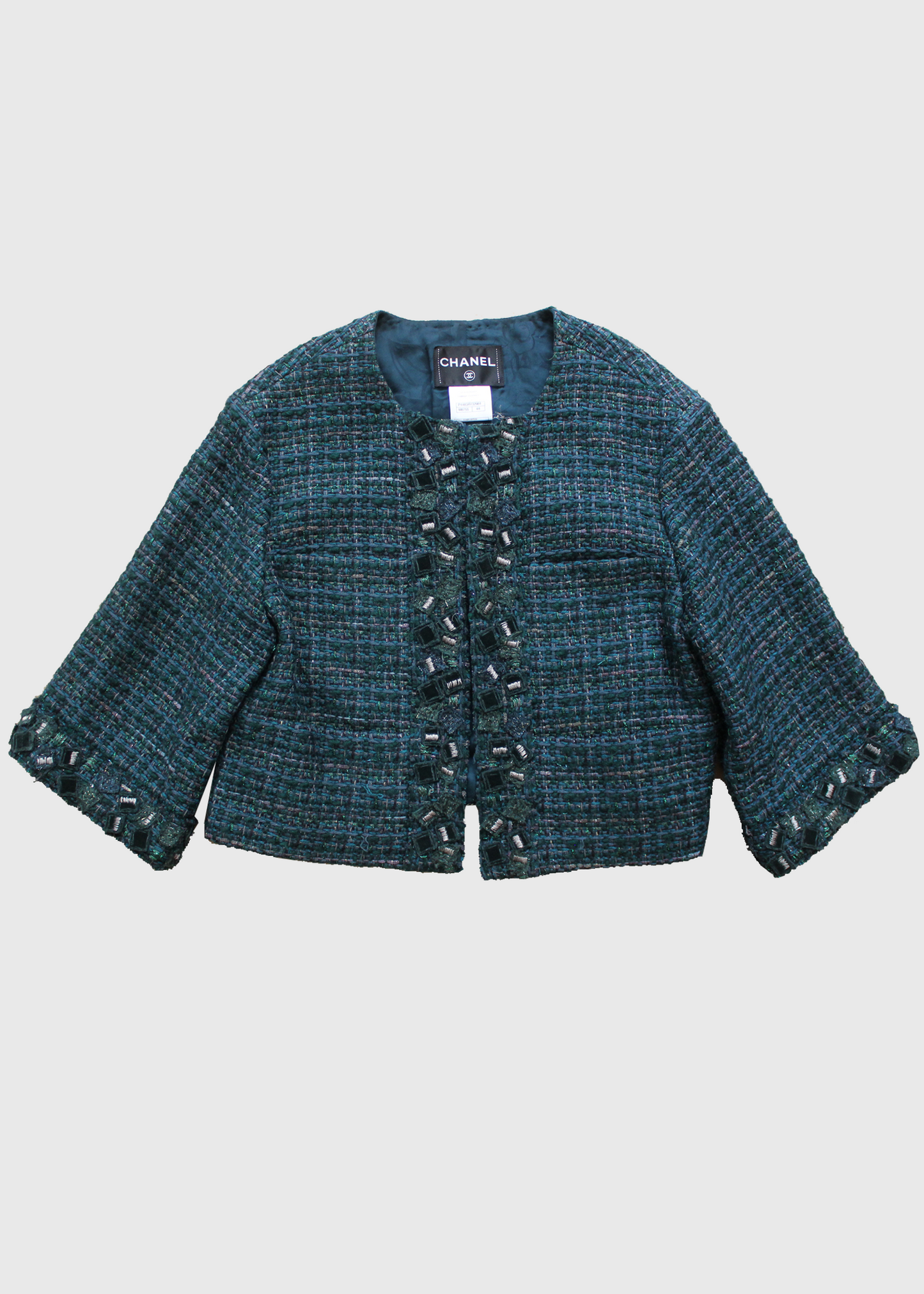 This is a Metallic deep sea green boucle tweed with 3/4 sleeves jacket by Chanel. Collarless with velvet and tweed embellishments. Lined in tonal Camellia printed silk and has a silver signature chain around the inside of the hemline. Front hidden hook closure