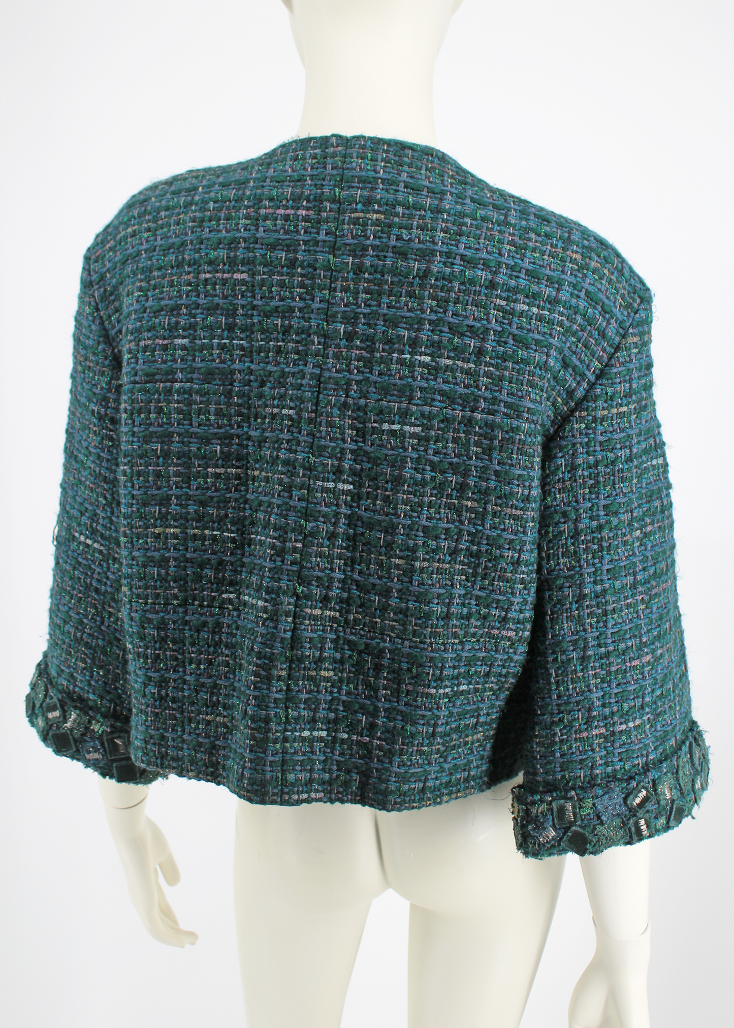 Back view of the metallic deep sea green boucle tweed with 3/4 sleeves jacket by Chanel. Collarless with velvet and tweed embellishments. Lined in tonal Camellia printed silk and has a silver signature chain around the inside of the hemline.