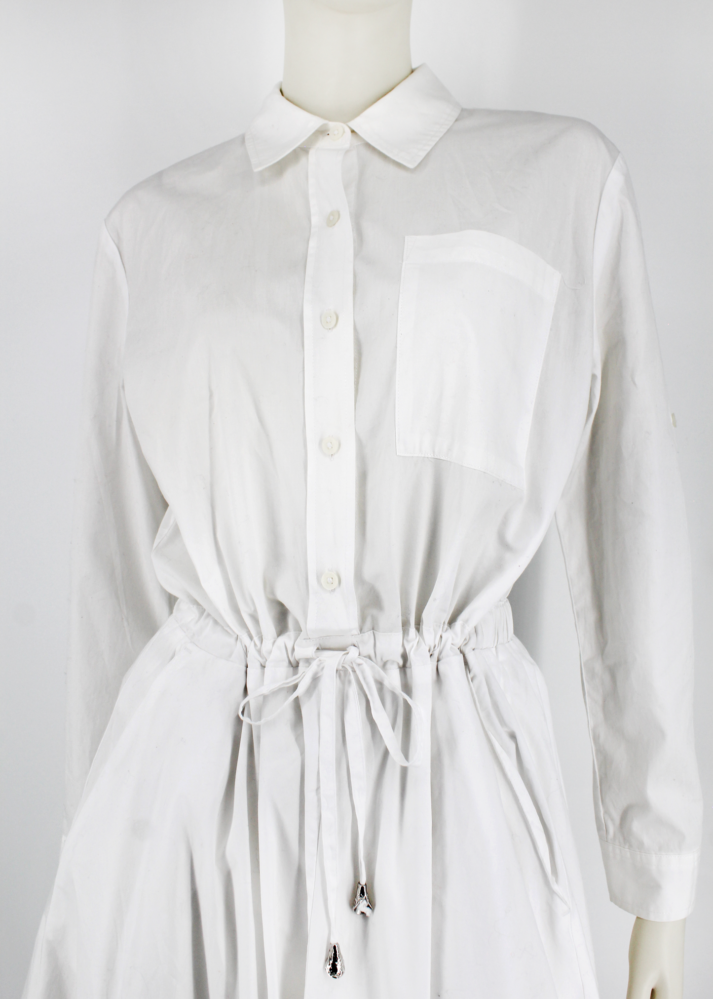 This is a white long sleeve button up t-shirt dress with a full skirt, adjustable tie waist, and Brest pocked detail.