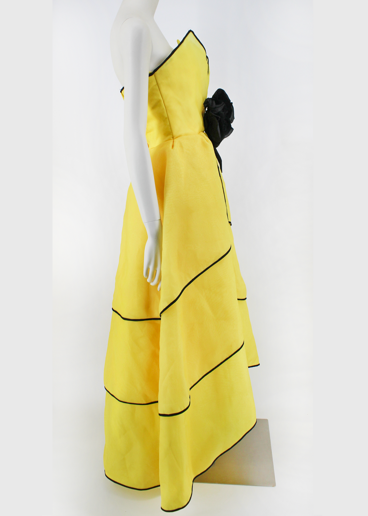 An absolutely breathtaking Victor Costa gown from the 1960s featuring layers of bright yellow organza, an architectural bodice, black piping along the hem of every layer of the dresses skirt and neckline, and an oversized black flower embellishment at front. Slightly higher in the front than in the back.