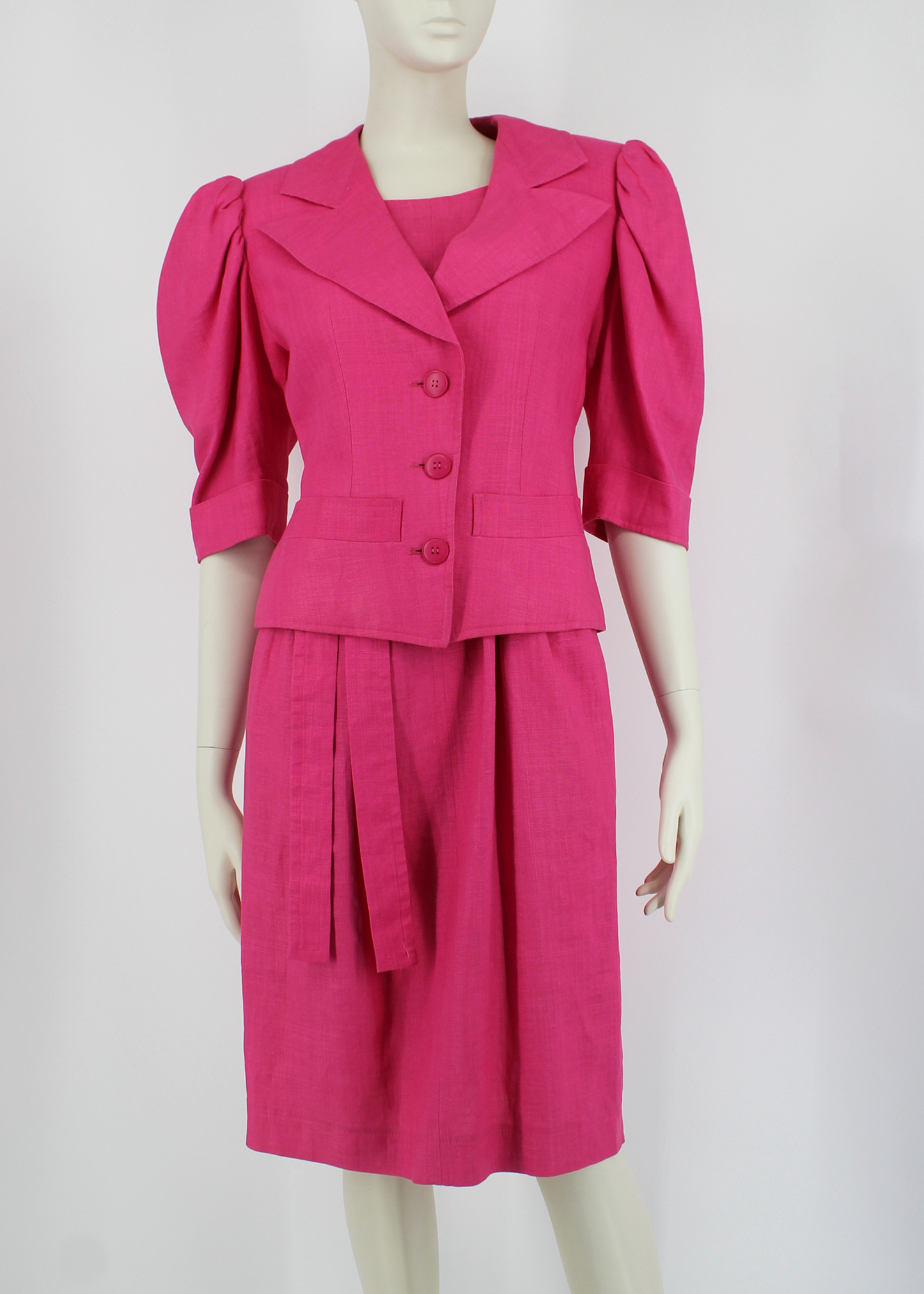 A fabulous, bright pink linen 2 piece set from 1985 Yves Saint Laurent. The dress comes includes a matching belt, knotted to one side and has button details at the back. The jacket has structured shoulders and puff sleeves and featured three matching round pink buttons and two pockets on its front bodice.