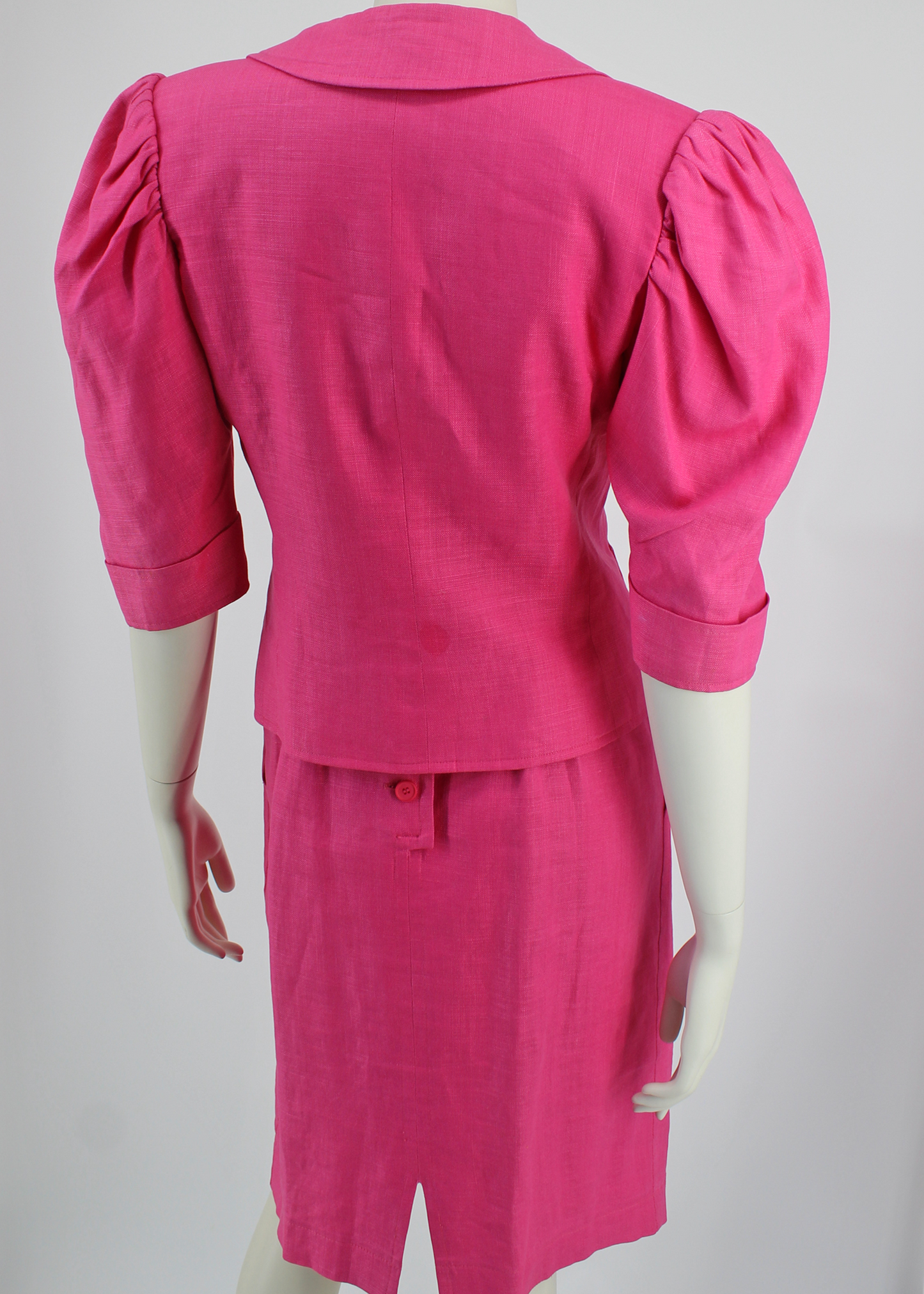 A fabulous, bright pink linen 2 piece set from 1985 Yves Saint Laurent. The dress comes includes a matching belt, knotted to one side and has button details at the back. The jacket has structured shoulders and puff sleeves and featured three matching round pink buttons and two pockets on its front bodice.