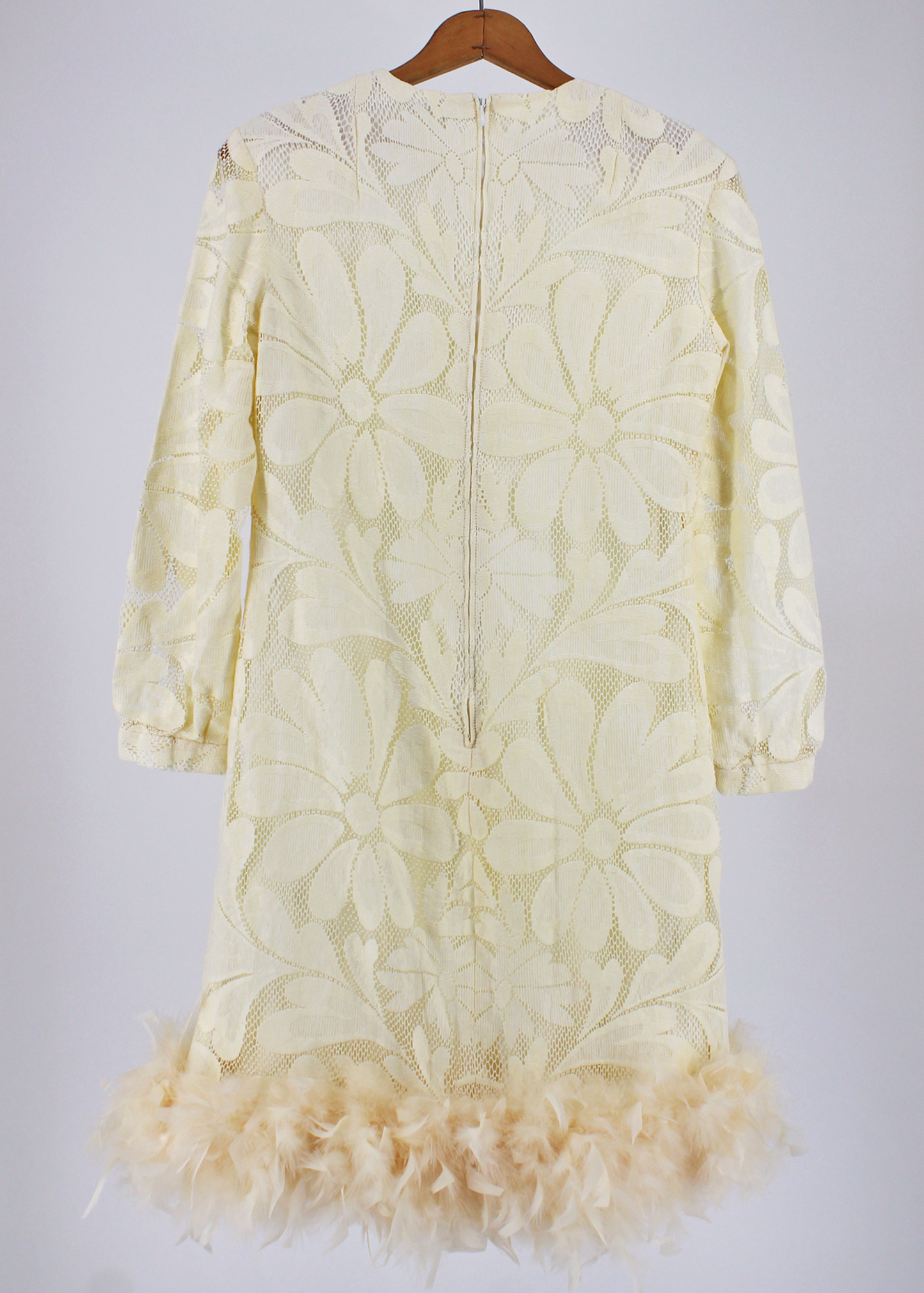 Beautiful 1970s ivory lace dress featuring an oversized daisy lace pattern, cuffed long sleeves, and a gorgeous sweep of ivory feathers at the bottom hem.