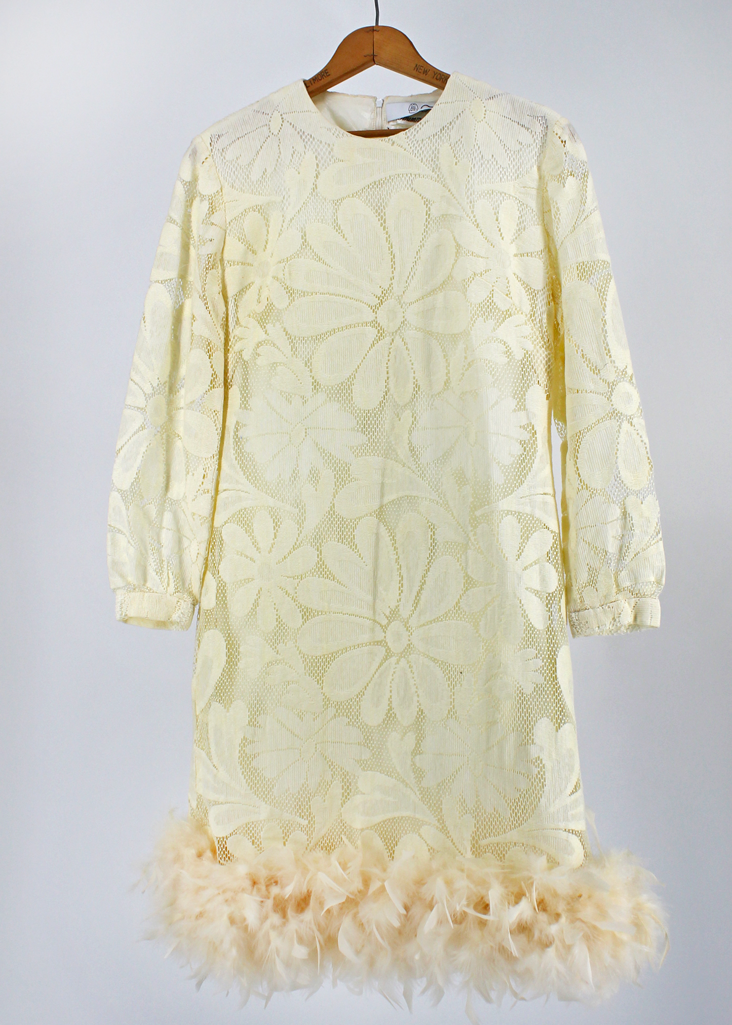 Beautiful 1970s ivory lace dress featuring an oversized daisy lace pattern, cuffed long sleeves, and a gorgeous sweep of ivory feathers at the bottom hem.