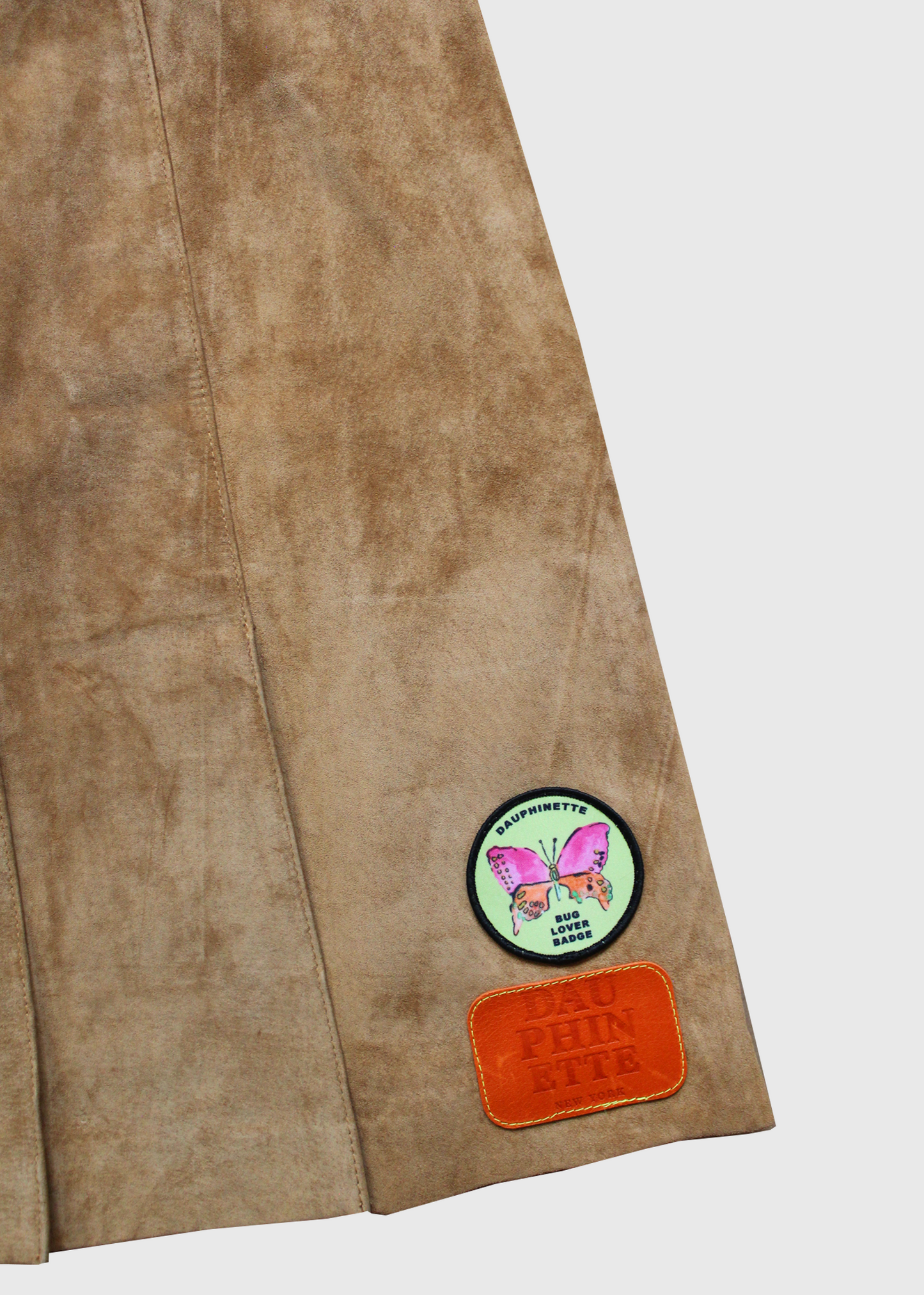 Camel suede pleated mini skirt with signature Dauphinette text and Dauphinette pink and green butterfly patches.