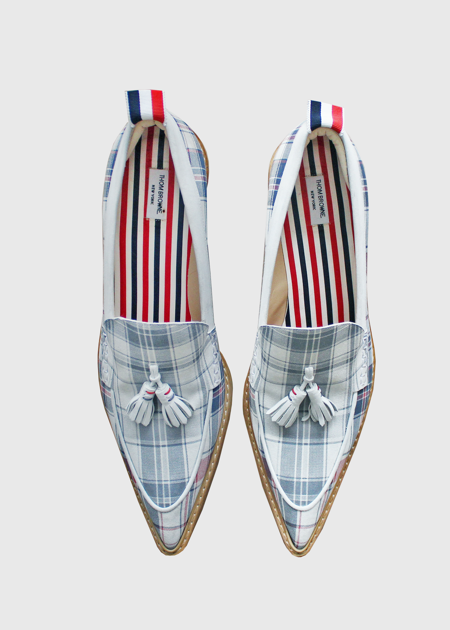 These Thom Browne shoes feature a very pointed toe, tassels, and a stacked, curved wooden kitten heel. Rendered in signature blue and white Thom Browne plaid and a red, white, and blue stripped lining.