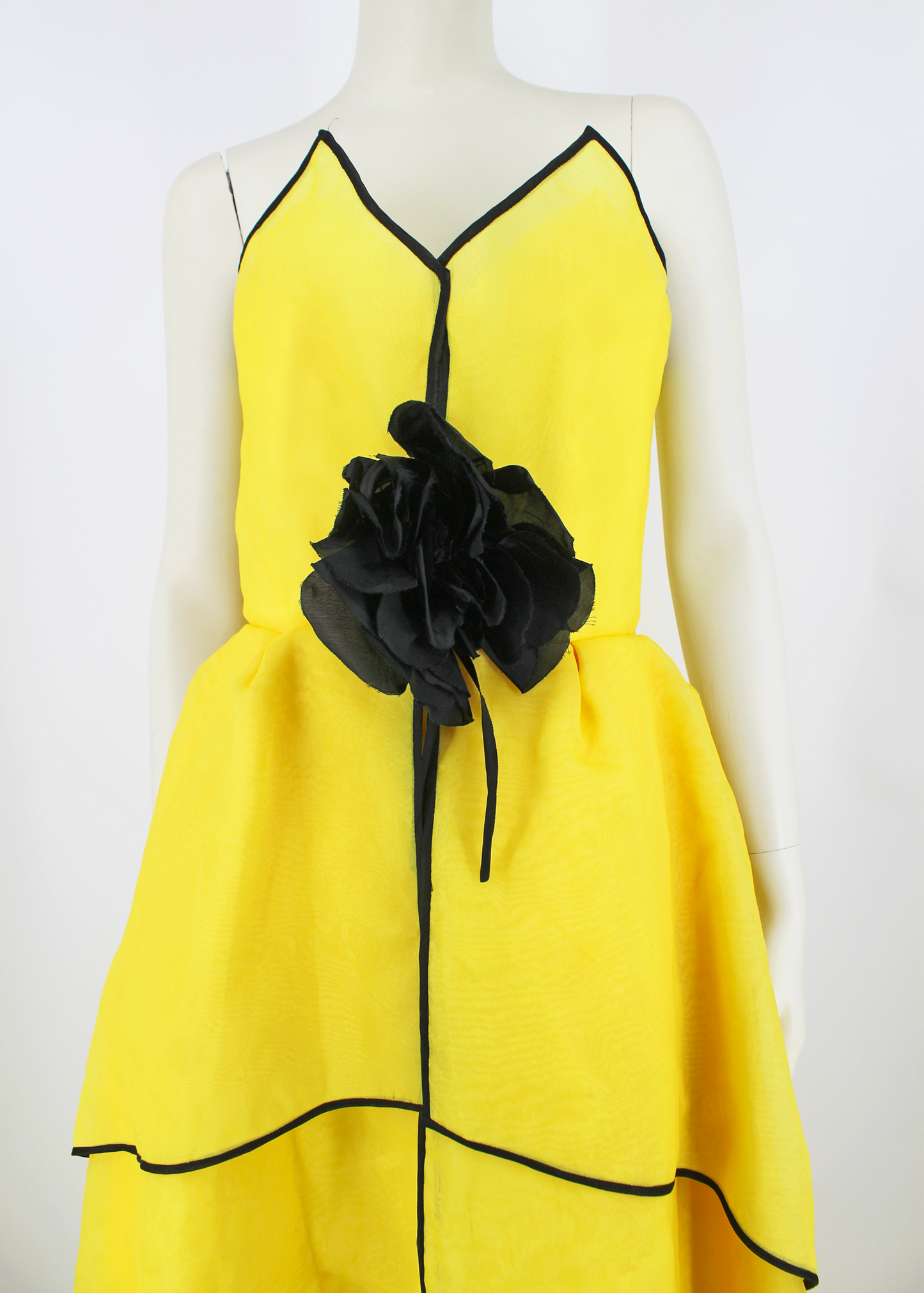 An absolutely breathtaking Victor Costa gown from the 1960s featuring layers of bright yellow organza, an architectural bodice, black piping along the hem of every layer of the dresses skirt and neckline, and an oversized black flower embellishment at front. Slightly higher in the front than in the back.